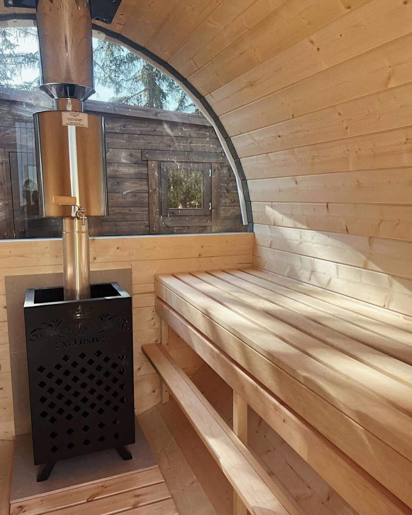 Interior view of a Terra Sauna barrel model showing the sunlight hitting the timber benches and a wood-burning stove.
