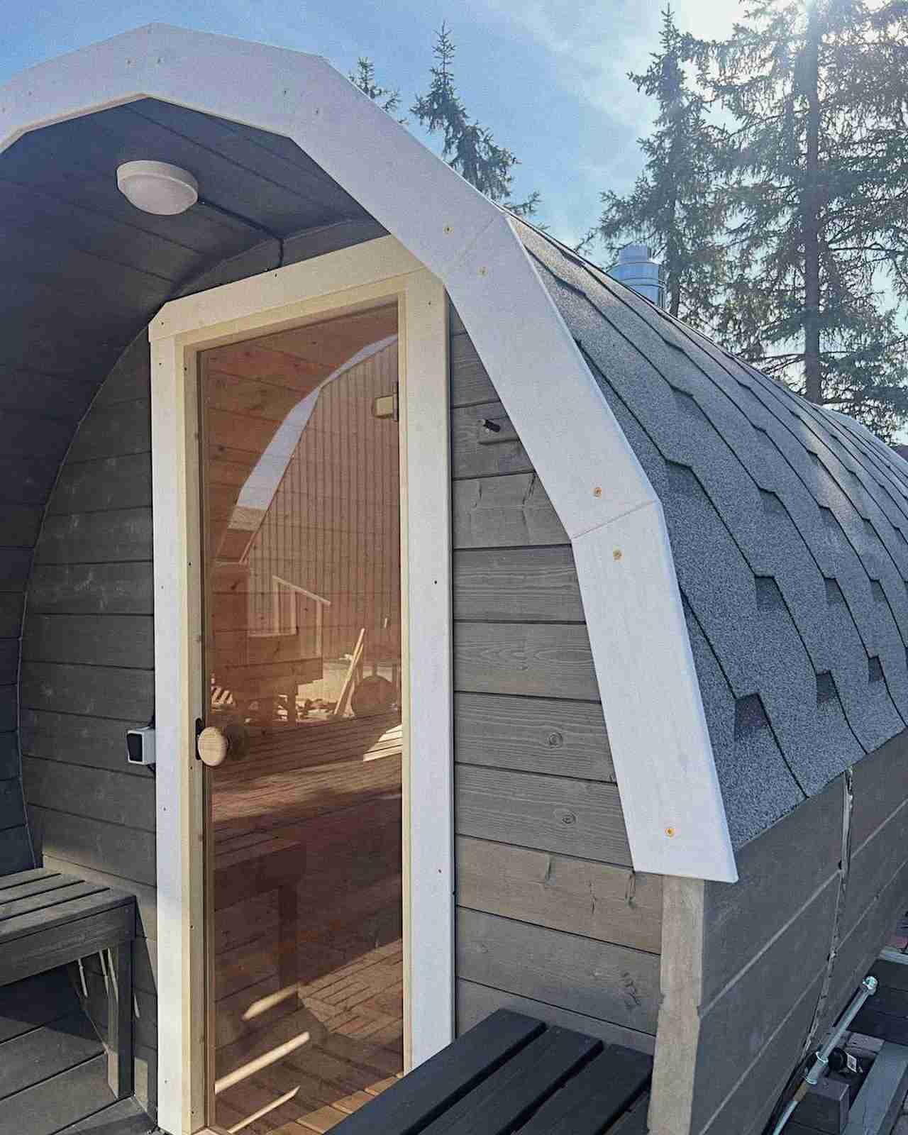 Close-up of a grey barrel sauna entrance featuring a glass door and white trim detailing.