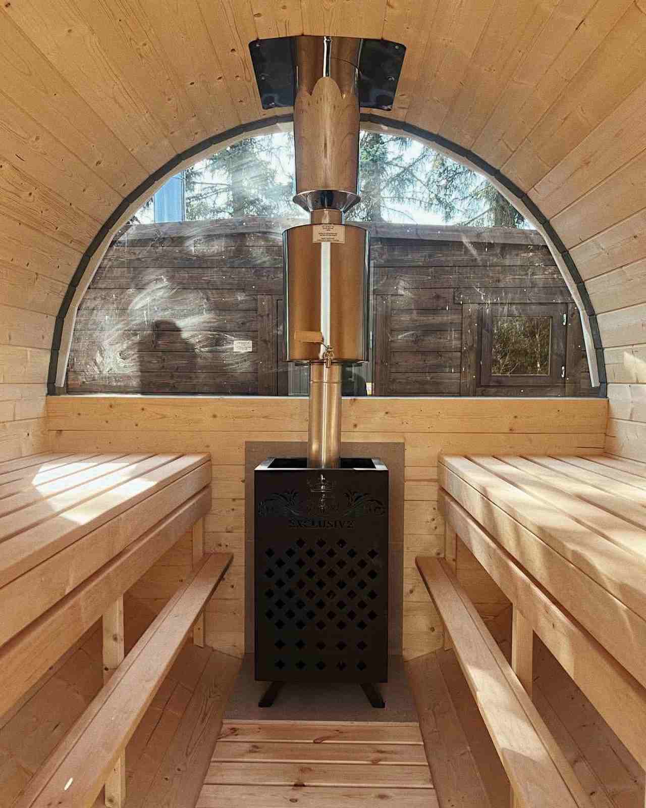 Symmetrical interior view of a barrel sauna with a wood-fired stove and large semi-circle window.