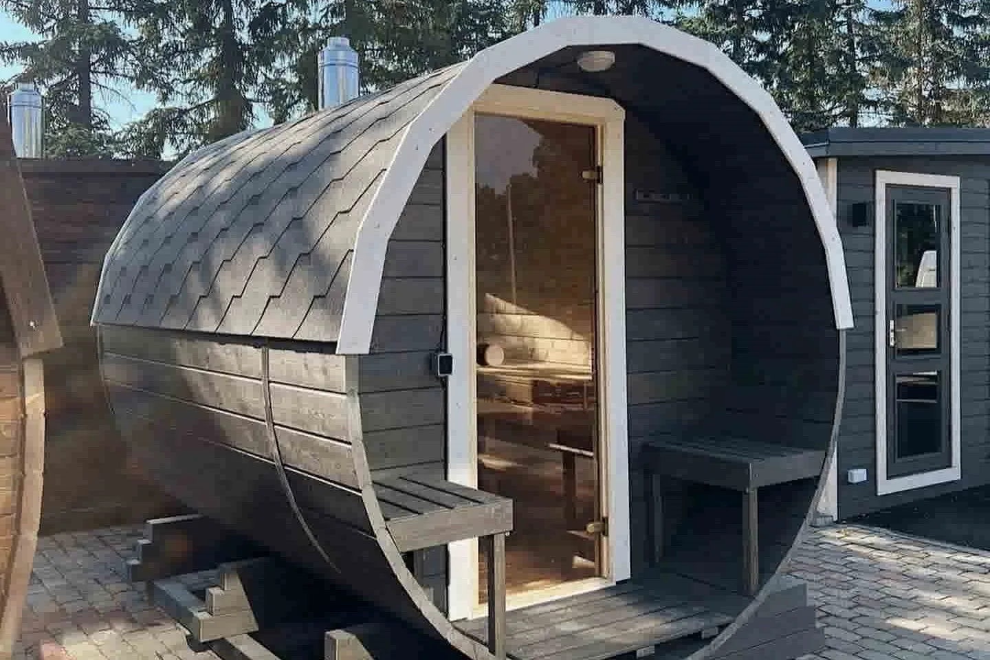 Handcrafted grey barrel sauna with white trim and shingle roof, representing our premium outdoor sauna sales in Guernsey.