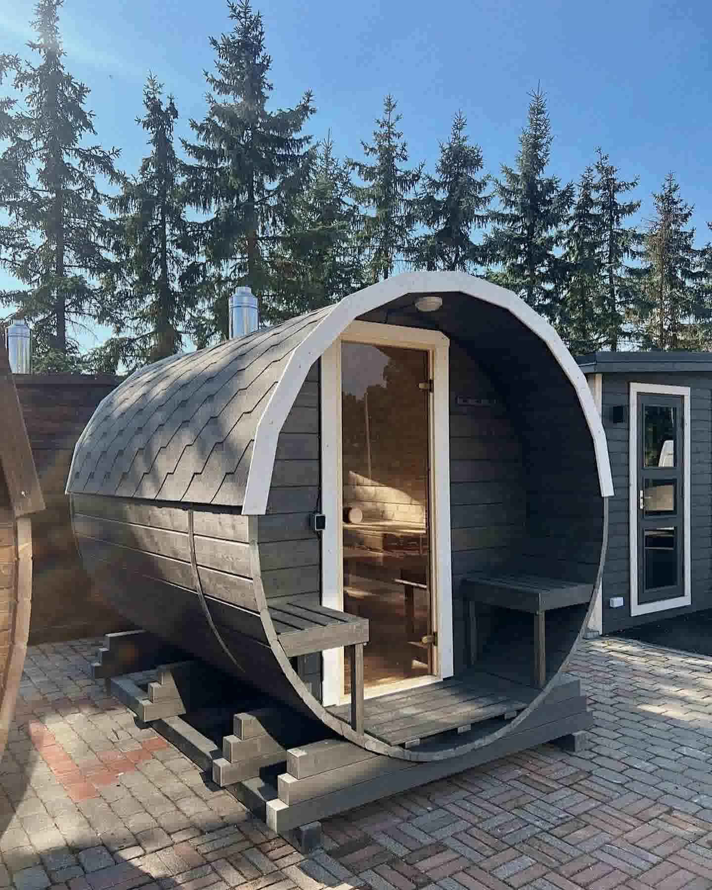 A full side profile of The Cadus horizontal barrel sauna, highlighting the artisanal wood-fired design and outdoor seating.